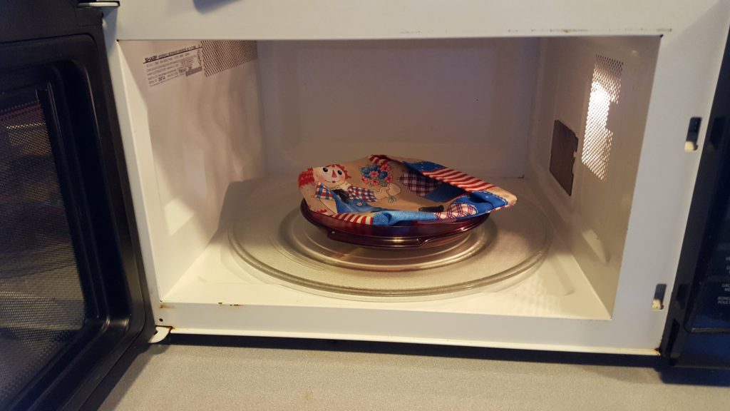 homemade reusable microwave popcorn bag on plate inside a microwave with door open