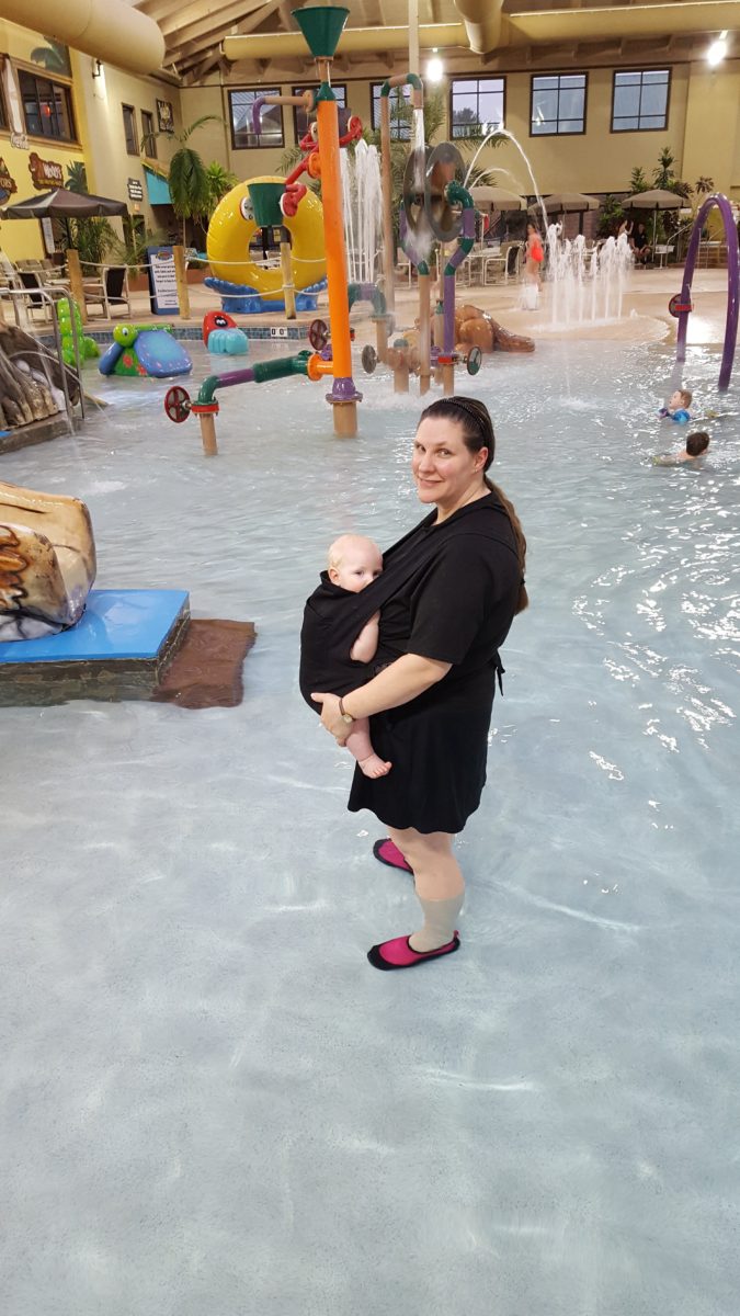Large Family Vacation mom and baby in a front carrier standing in shallow water indoor waterpark