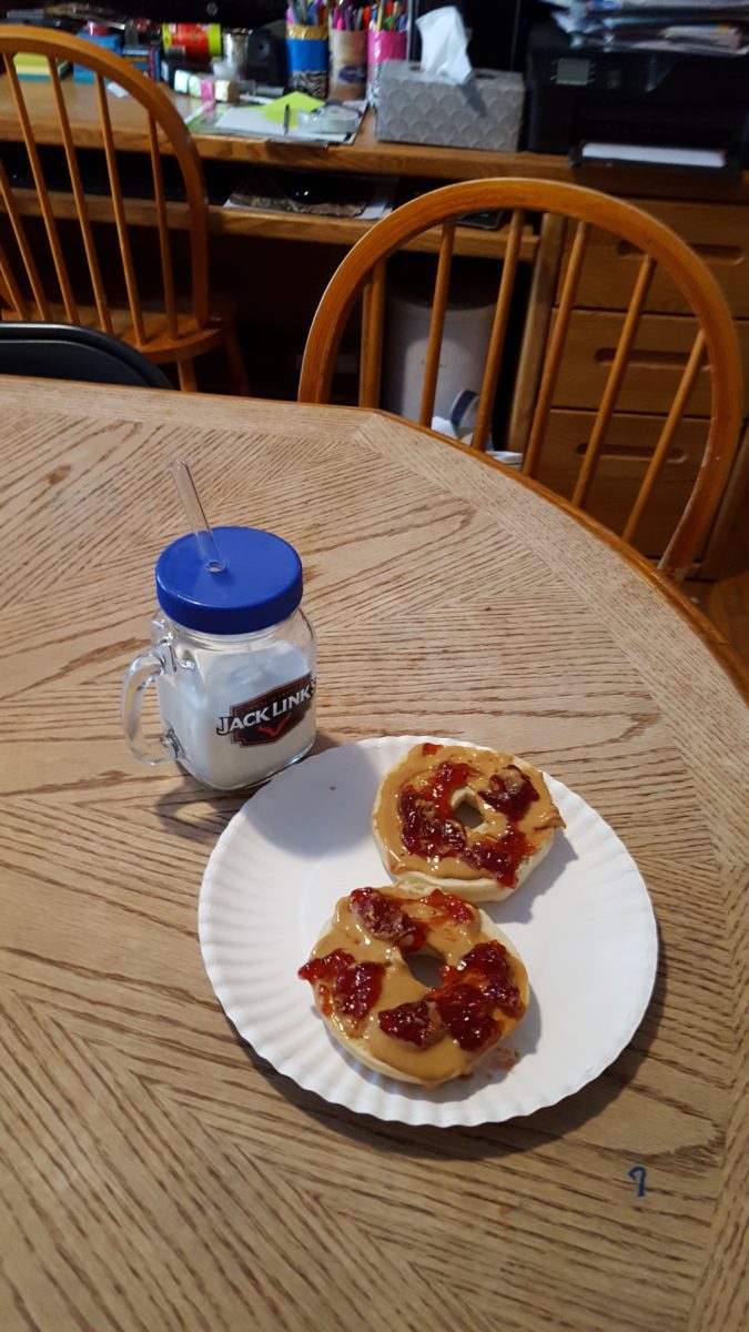 milk in a glass jar with a glass straw and bagels with peanut butter and jelly