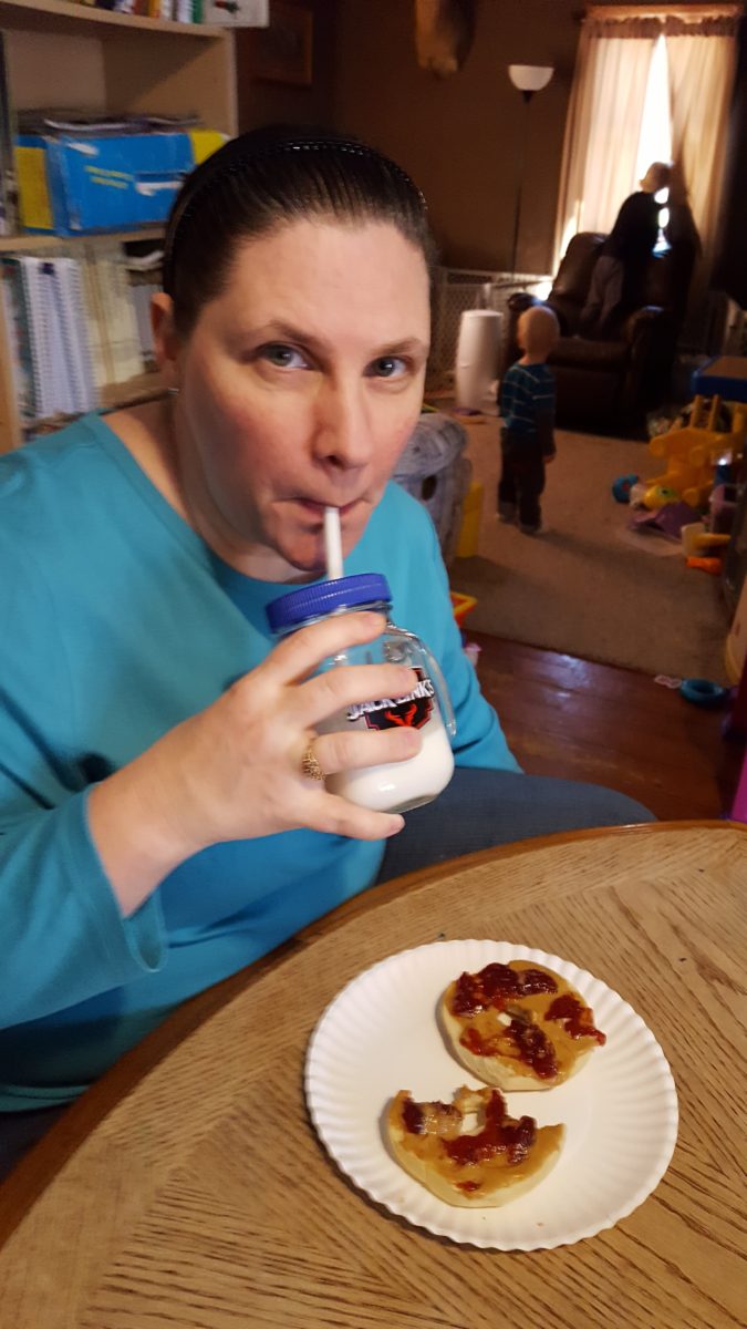 a woman drinking milk through a glass straw with pb&j bagels on the table