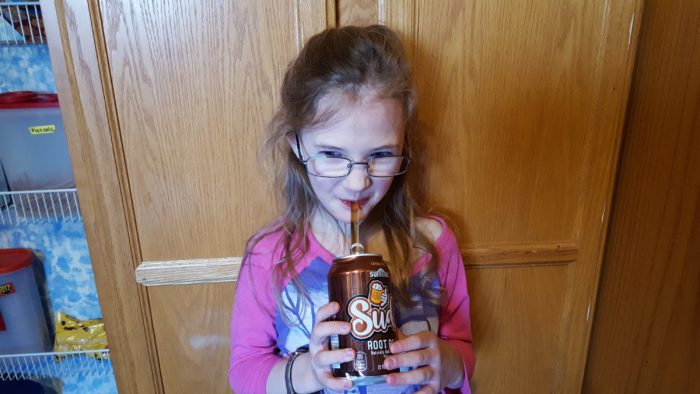 a young girl drinking root beer from a glass straw