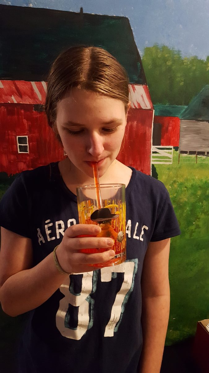 a teen girl drinking from a glass straw out of a glass