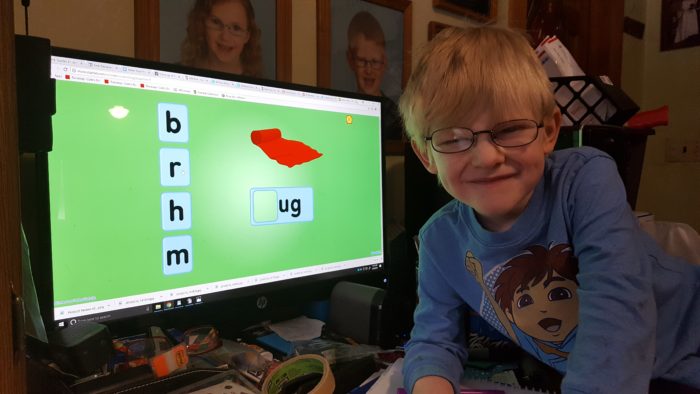 a blond boy in glasses using the starfall online reading program on a desktop computer