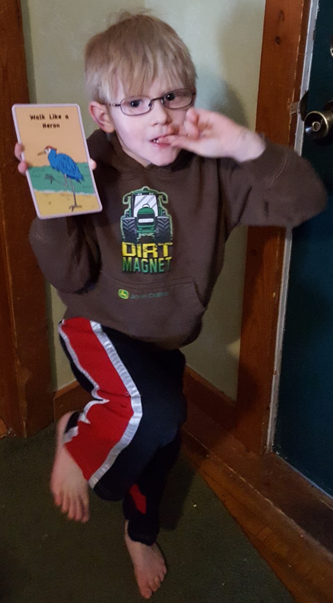 boy with one foot in air and finger in mouth wearing glasses and holding a card walk like a heron haley sez