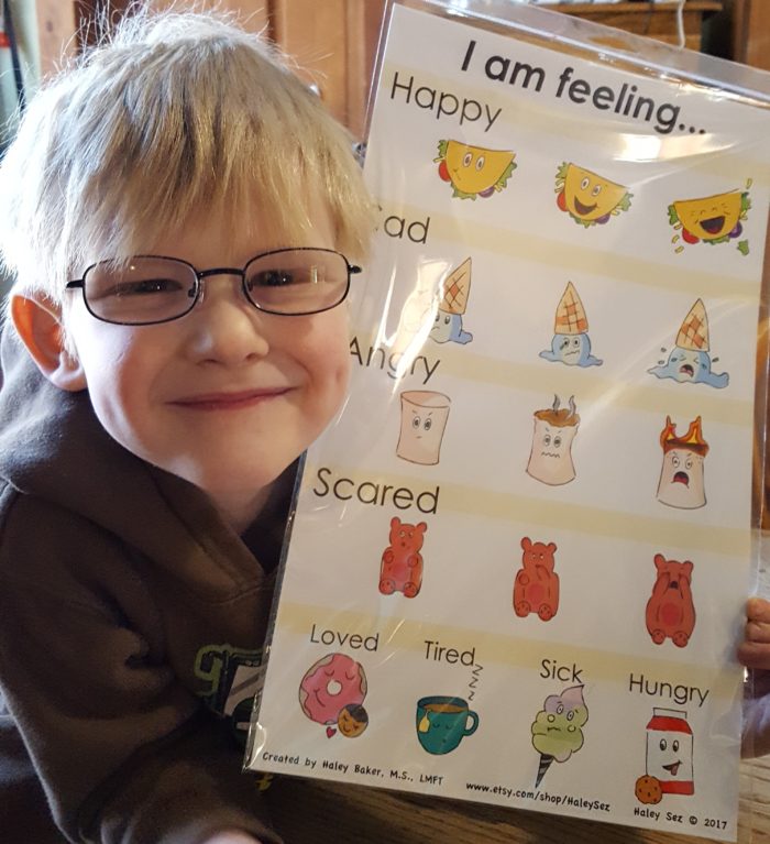 blond boy with glasses smiling dimples happy holding i am feeling chart from Haley Sez happy sad angry scared loved tired sick hungry