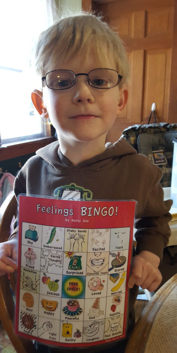 blond boy with glasses holding a feelings bingo card from haley sez