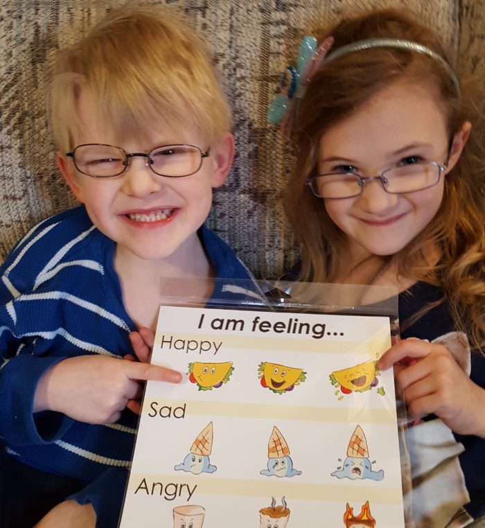 boy and girl wearing glasses smiling holding feelings chart happy from Haley Sez