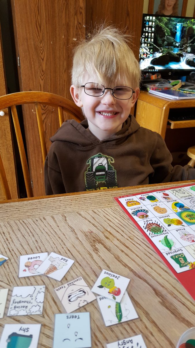 young boy with glasses smiling playing a game of Haley Sez Feelings BINGO!