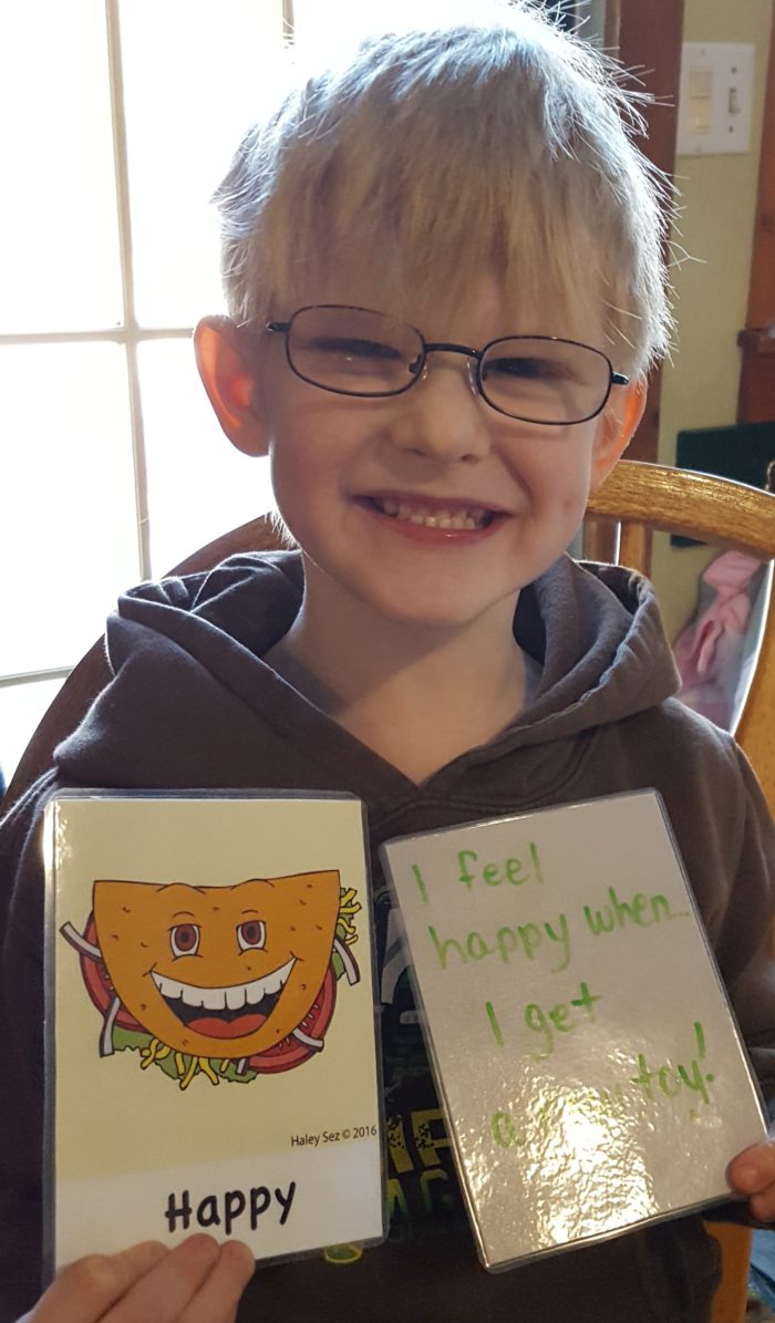 young boy glasses holding happy feeling taco and card that says i feel happy when i get a new toy haley sez