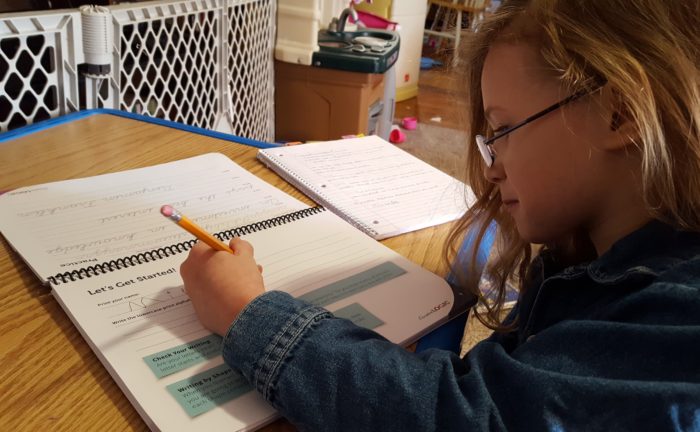 a girl in glasses writes left handed in the cursive writing workbook with the cursivelogic program