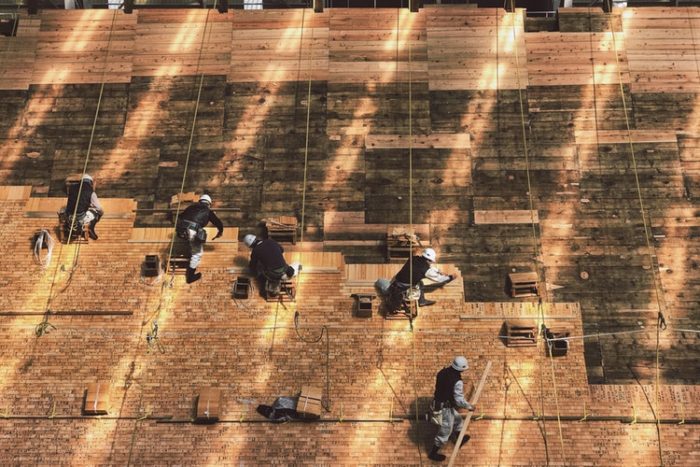 five men building a roof on a large building using quality wood materials