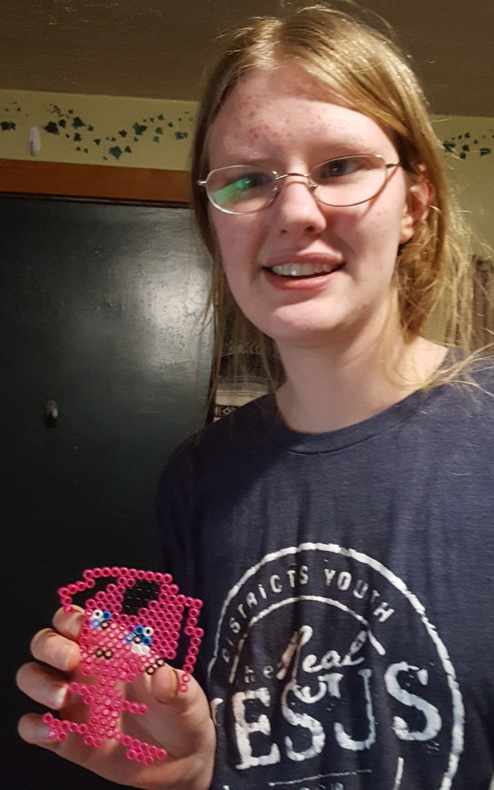 Teen girl with blond hair and glasses hold up her impression of Miraculous Ladybug's friend, Tikki that she made using Zirrly Super Beads for a product review