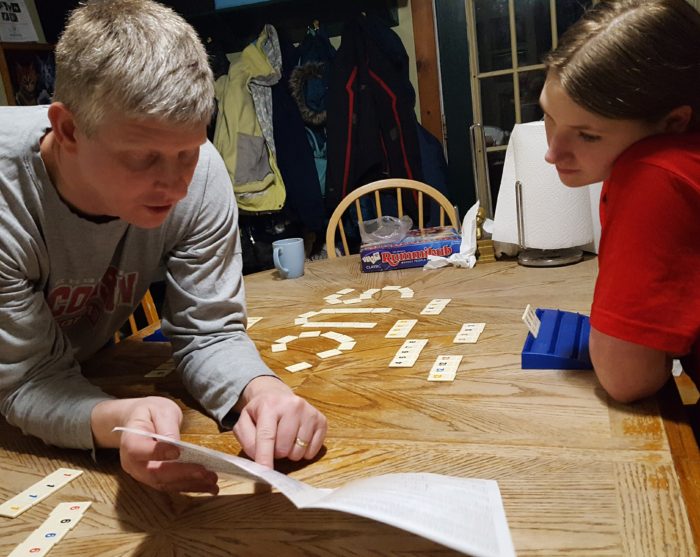 Dad reading rules to his teen daughter playing Rummikub