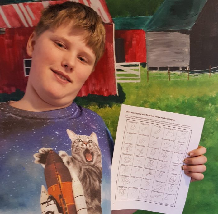 a teen boy showing his snow shape drawings from a homeschool unit study on snow