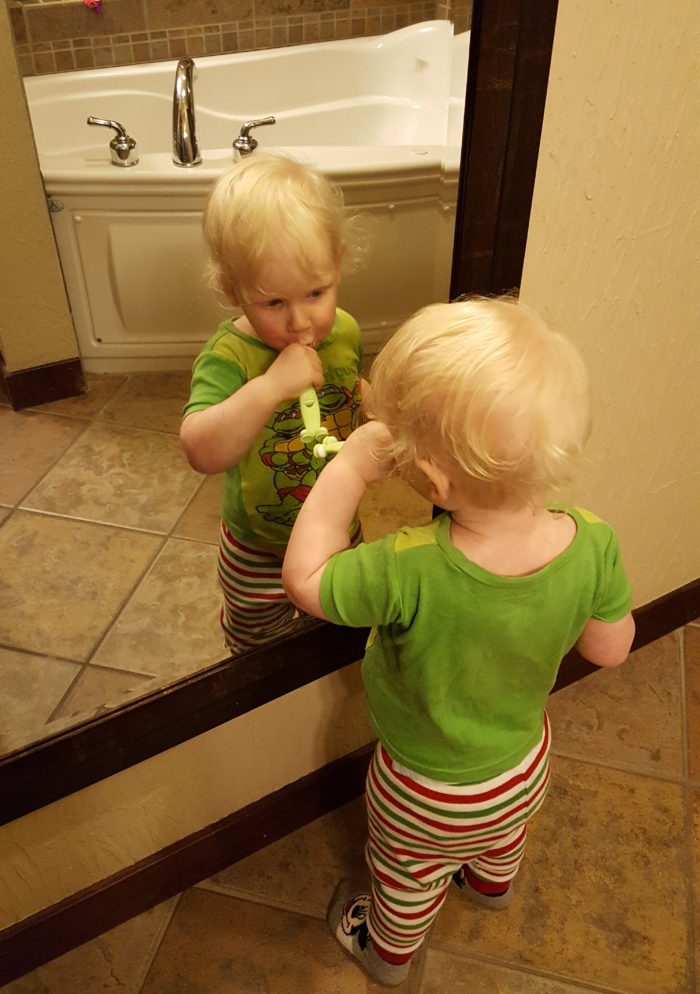 Toddler boy brushing his teeth in front of a mirror with no care of germs thanks to IntelliDent Toothbrush Shield