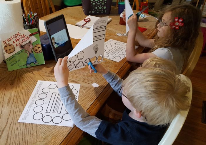 Home School Navigator image of children at a table cutting worksheet pages while watching iPad video for Level Red