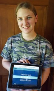 Geology and Apologetics teen girl holds electronic tablet with online geology class for high school