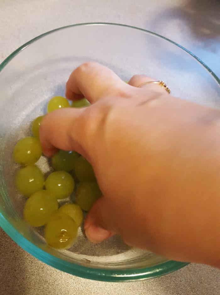 Young Living Thieves Products hand mixing fruit wash into grapes 