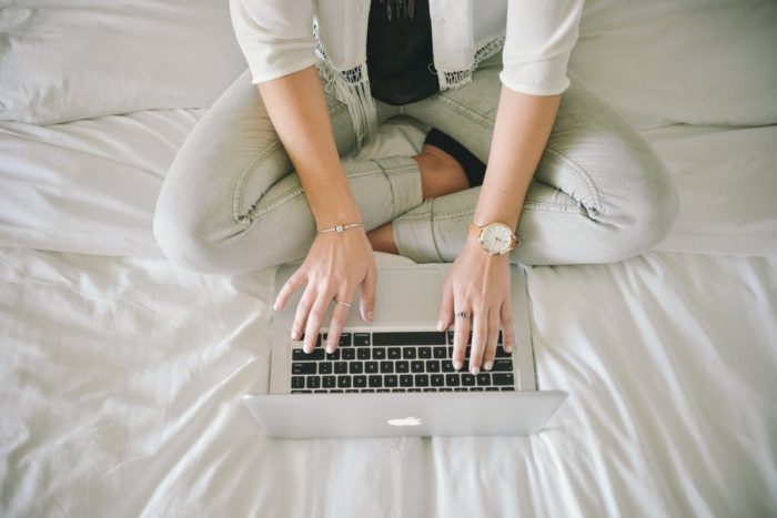 Great reasons to work from home woman sitting on bed typing on laptop