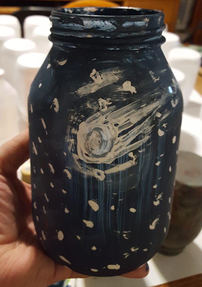 Mason Jar Crafts hand holding a painted mason jar to look like a fantasy night sky with a shooting star or comet
