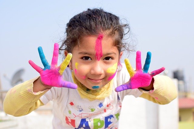 Hobbies for children - girl fingerpainting colorful paint on child's face and hands