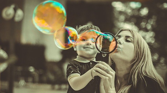 Parenting is not easy mom blowing large bubbles while holding small son