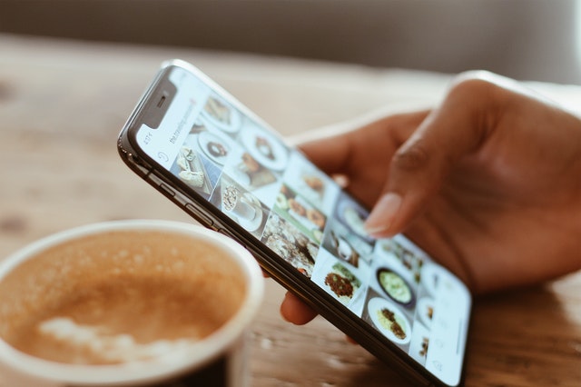 social media break hand holding smartphone with images of food cup of cocoa