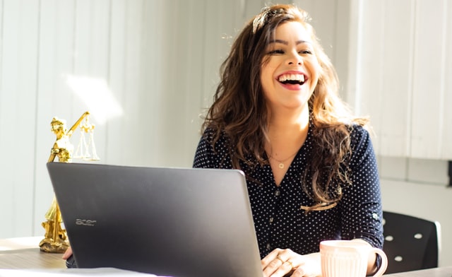 ecommerce enterprise owner smiling and laughing behind laptop as she is doing well with sales