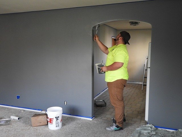 major home repairs less expensive a man painting his drywall a dark gray color in living room entryway