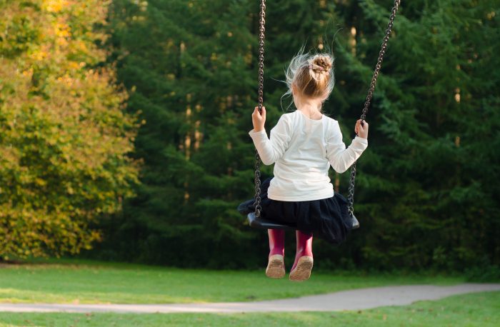 raising healthy children girl in swing playing outside summer green trees background