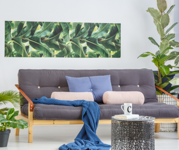artificial plants in living room next to sofa coffee table book mug pillows blanket wall decor