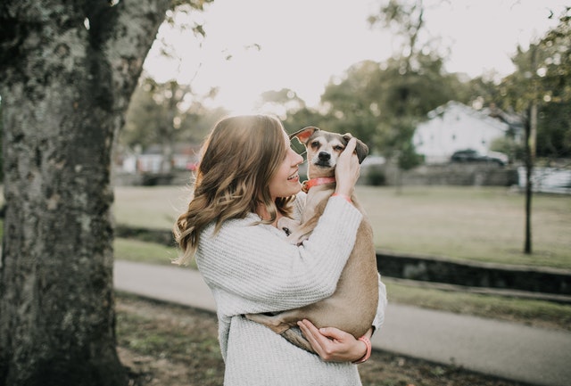 never owned a pet before smiling woman holding new dog outside next to tree trunk