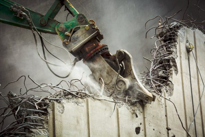 demolishing your home heavy equipment arm tearing apart a cement wall