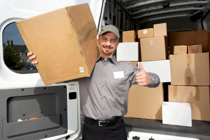 moving company family business man holding cardboard box with thumbs up in front of loaded moving van