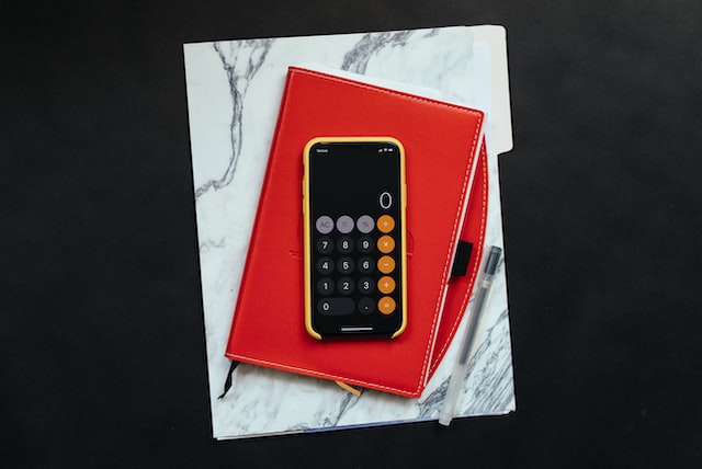 improve invoicing smartphone with calculator screen on a leather planner next to pen