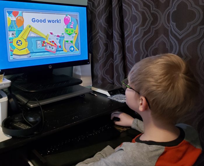 siblings busy homeschool boy using homeschool+ program on computer with words good work on screen