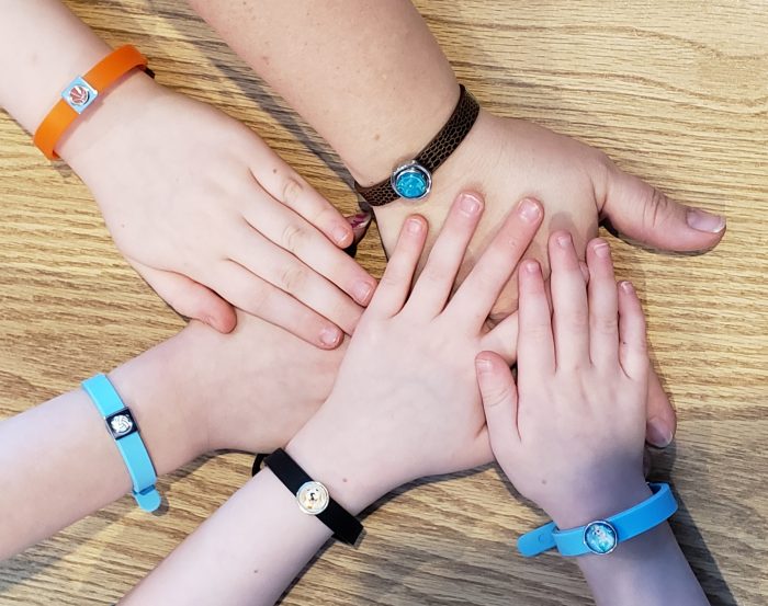 family magnetic bracelets on mom and four kids wrists putting their hands together on a brown wood table