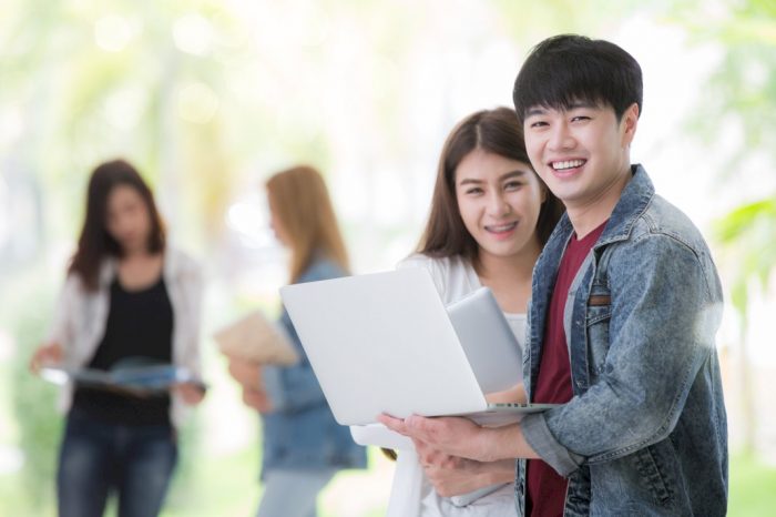 save money studying abroad smiling college students holding laptops and books