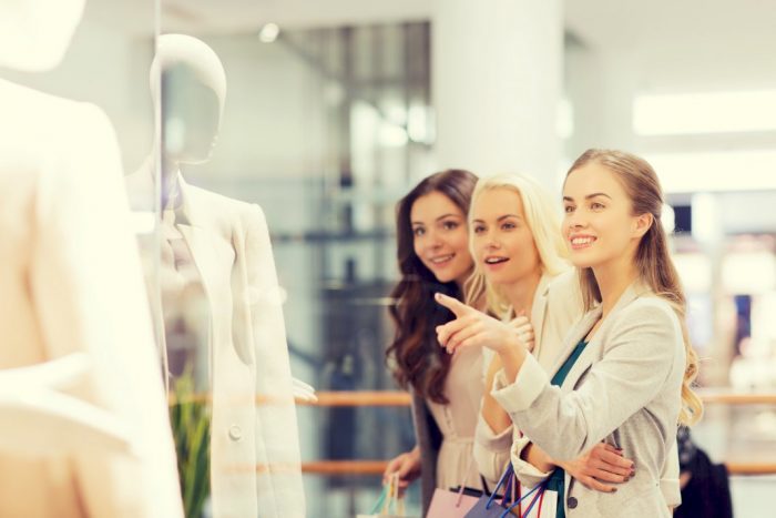 your company more visible three women pointing at clothing on mannequin in store window