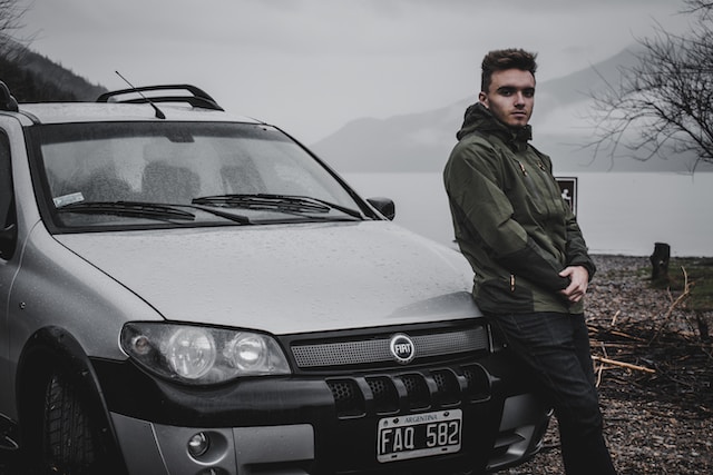 checks new car owner perform man standing next to new car with lake in background