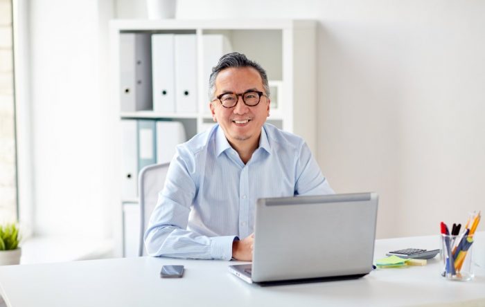 companies reach wide audience smiling man with glasses sitting behind laptop
