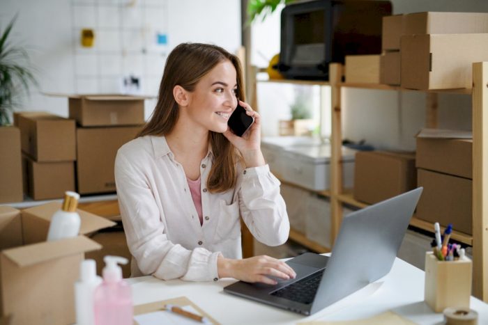 woman on cell phone smiling with laptop and boxes for home based business