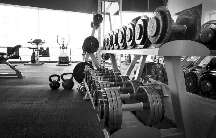 black and white photo of dumbbells on a rack and exercise equipment in a sun room of a home that decided to build a home gym