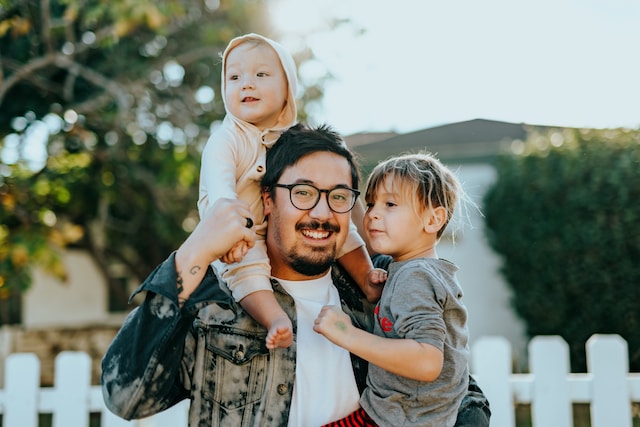 father with toddler on shoulder carrying preschool boy wanting to develop strong values in family