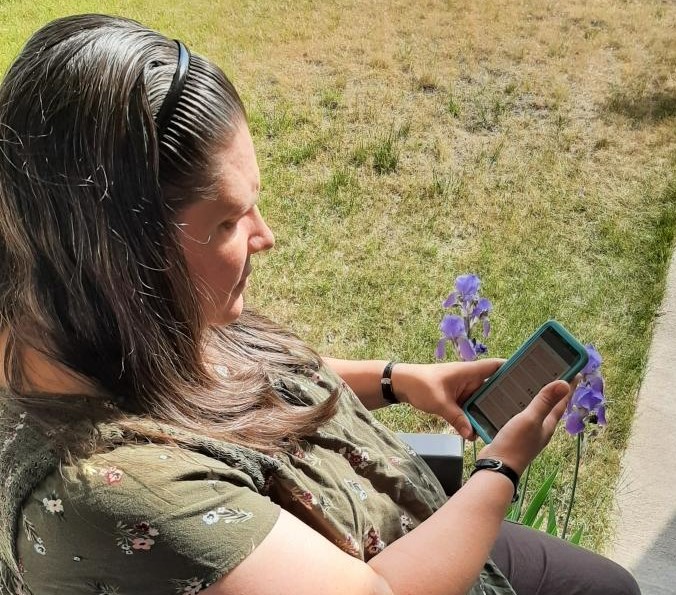 woman sitting outside next to flowers looking at her family calendar sharing app on her smartphone