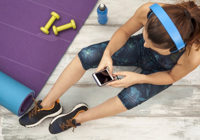 woman next to exercise mat and barbells looking for a home physical activity video on her phone