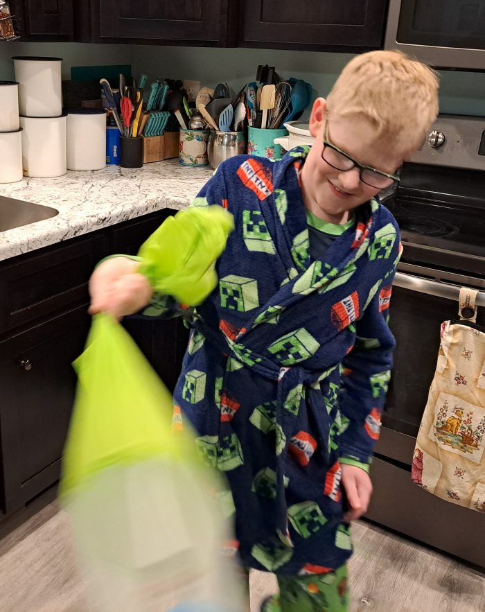 a boy wearing glasses smiling as he whirls the saladzilla salad spinner in the kitchen