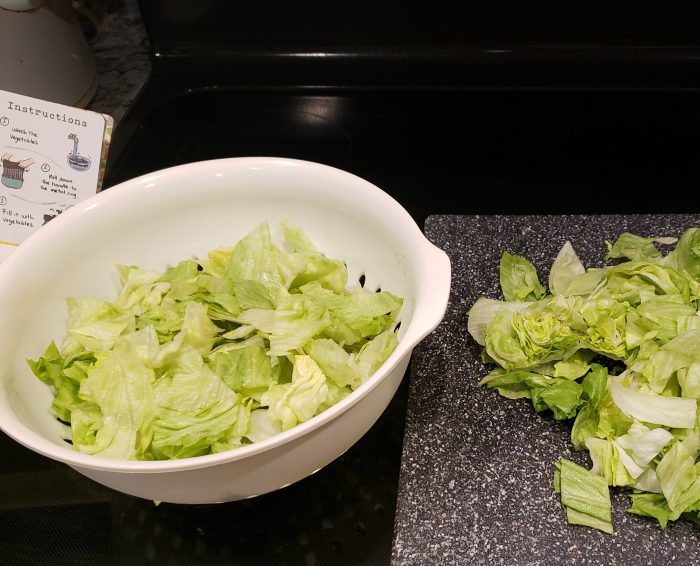 chopped lettuce in a plastic colander and on a cutting board with instructions to saladzilla salad spinner on the side