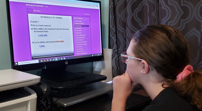 girl wearing glasses looking at computer screen in online math curriculum that says numerals in words