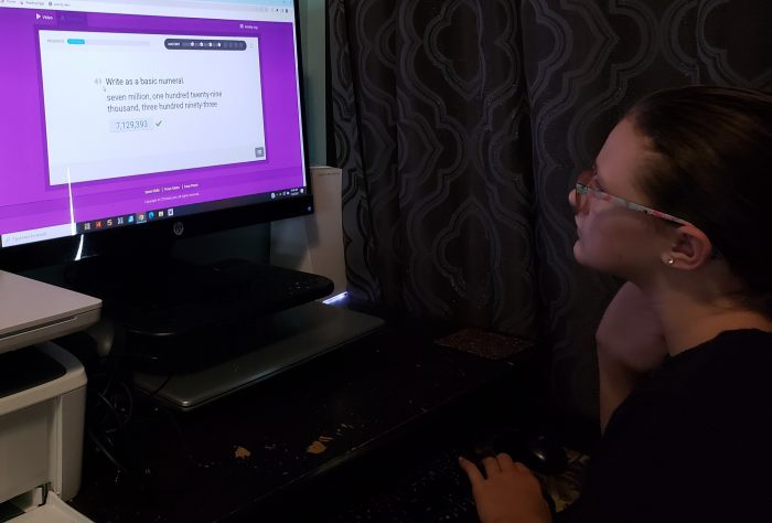 girl wearing glasses looking at computer screen for online math curriculum and typing on the keyboard